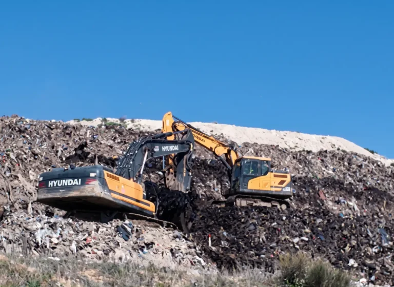 Two orange Hyundai excavators working on a landfill mound under a clear blue sky.