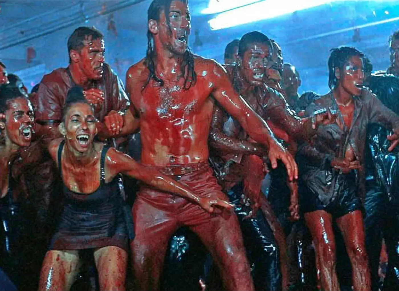 Group of people with red body paint dancing energetically in a dark, blue-lit club.
