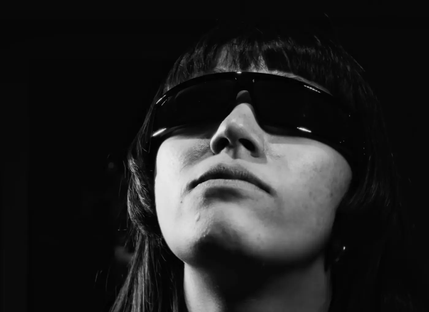 Close-up of a person wearing a large black visor over the eyes, looking upward in a grayscale photo.