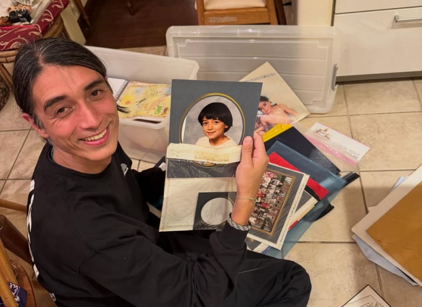 Smiling person sitting on the floor sorting through a collection of vinyl records and photo albums in a home setting