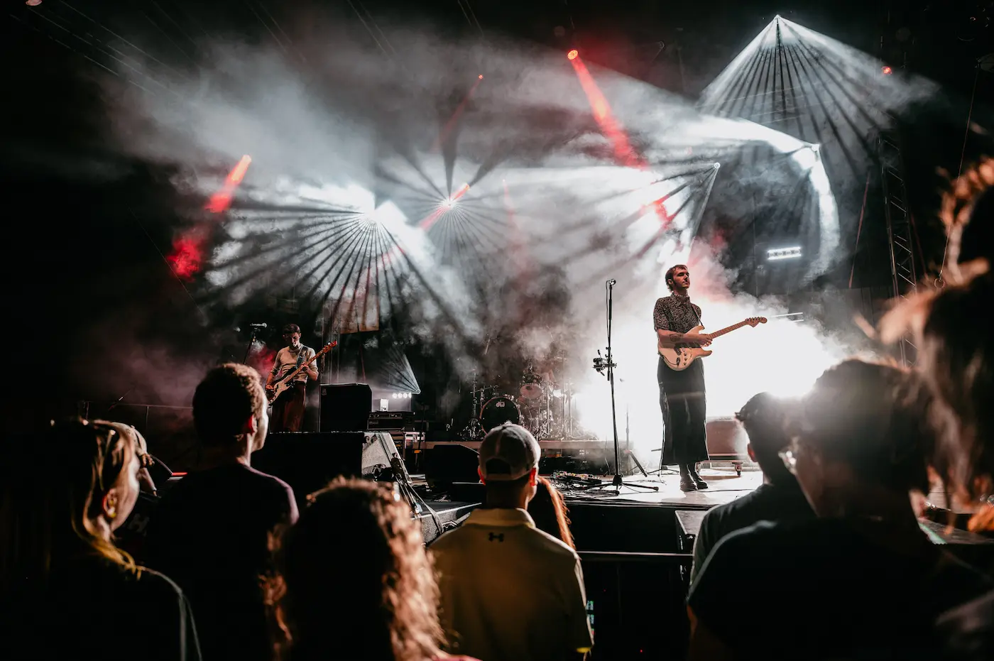 Guitarist singing into a microphone on a smoky concert stage with red and white lights.