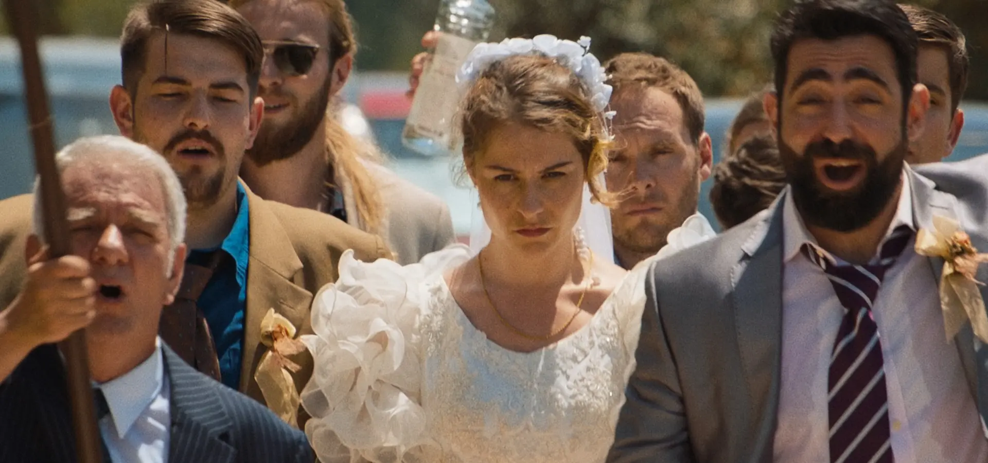 Bride in a white lace dress with a flower crown walks with her wedding party outdoors.