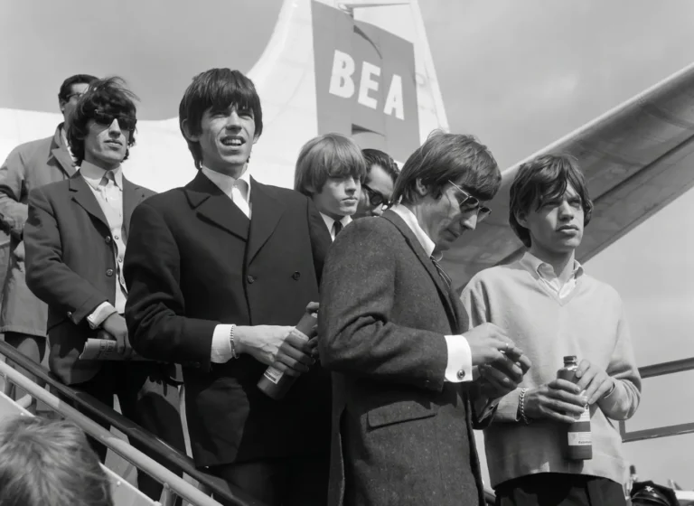 Group of young men in suits on airplane stairs, holding bottles, with a BEA tail in the background.