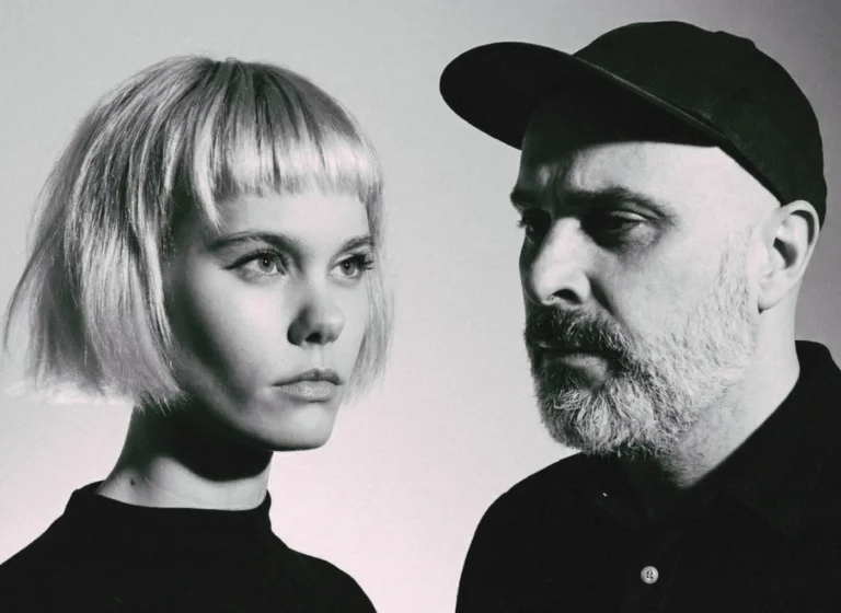 Black-and-white portrait of a woman with a short blonde bob and a bearded man wearing a cap facing each other in profile.