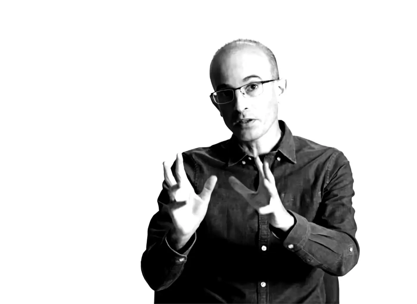 Black-and-white photo of a man wearing glasses, gesturing with his hands as if explaining something.