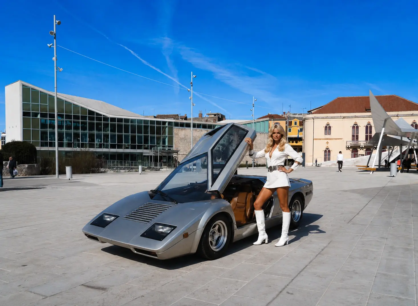 Blonde woman in a white outfit posing with a silver sports car with its door open in a sunny city square.