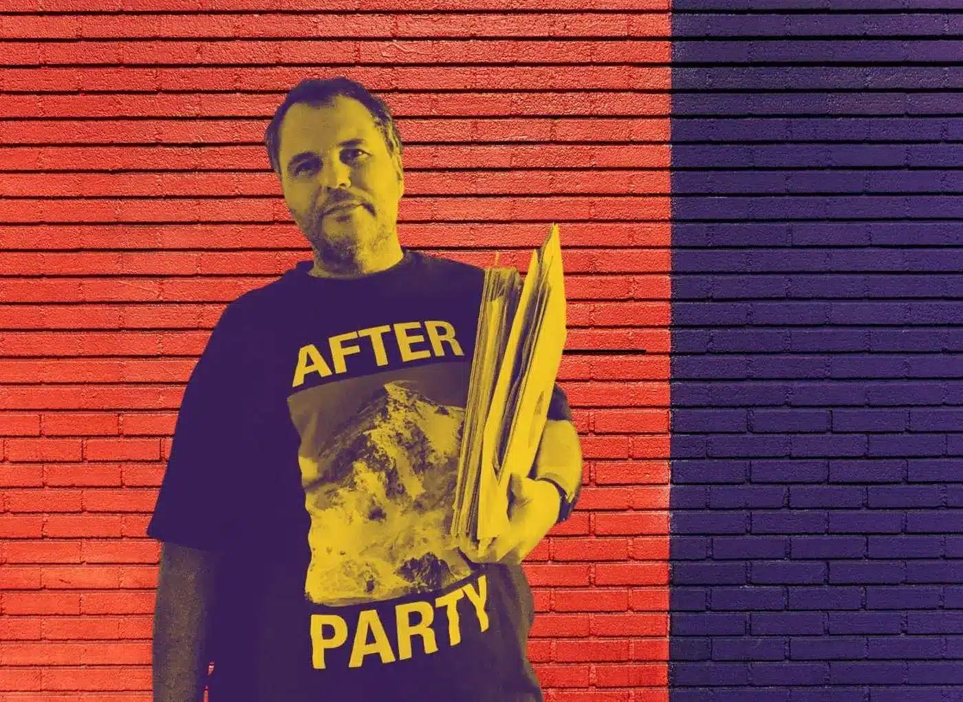 Man standing against a red-and-purple brick wall wearing a black T-shirt that says 'AFTER PARTY' and holding a stack of papers.