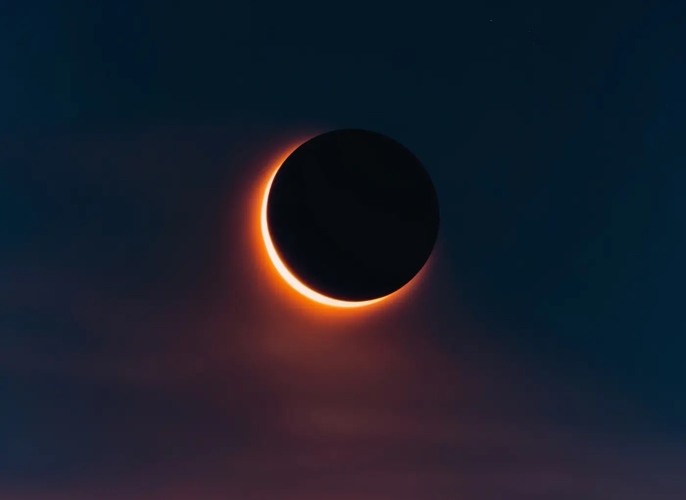 Total solar eclipse: dark Moon occludes the Sun, corona glowing orange against a night sky