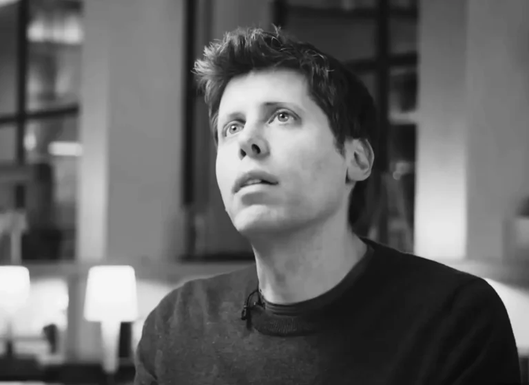 Black-and-white portrait of a man with short hair looking upward, wearing a dark sweater, indoors in a softly lit setting.