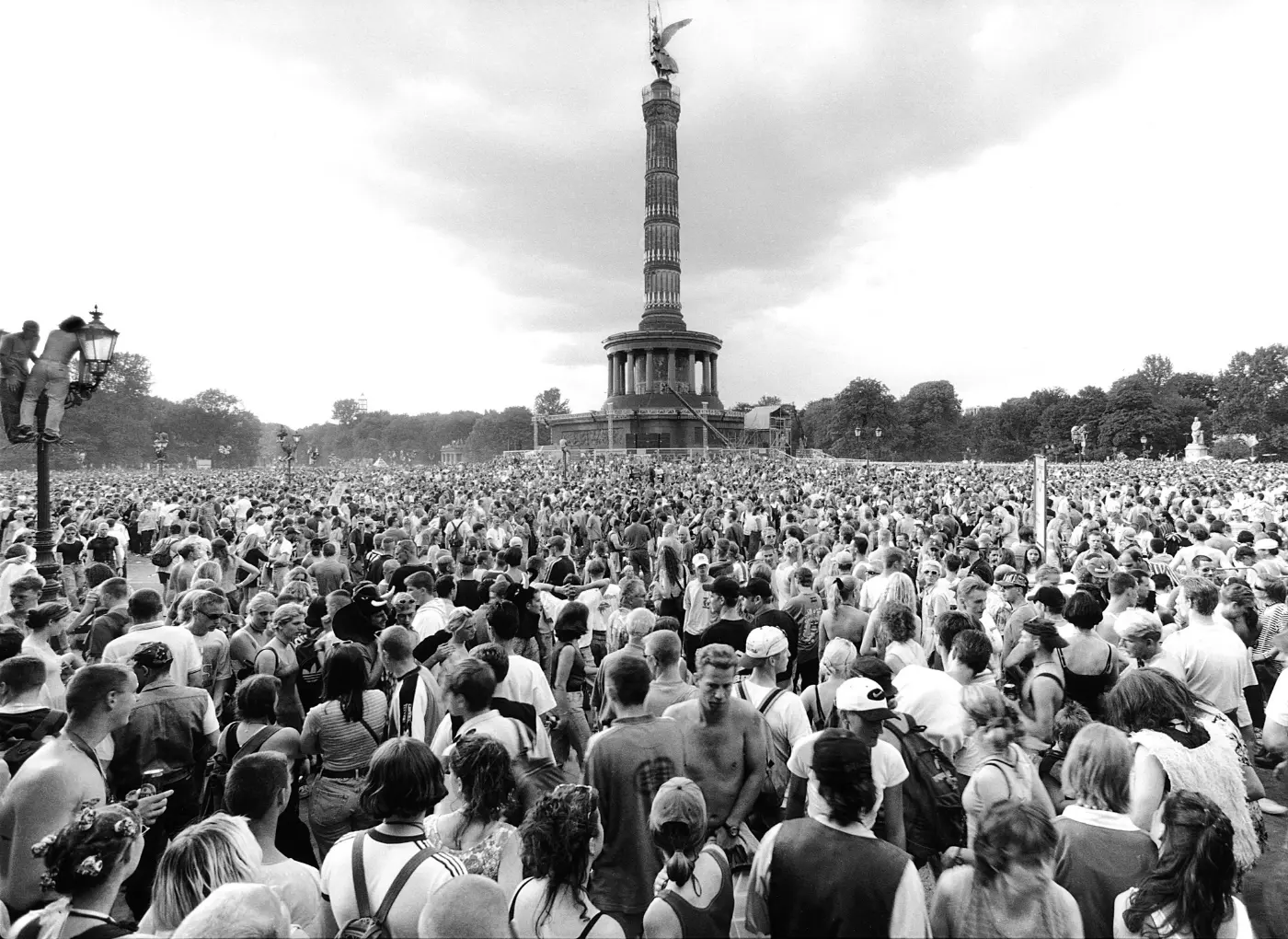Large crowd gathered in front of the Berlin Victory Column during an outdoor festival or event, with the monument rising in the center and trees in the background.