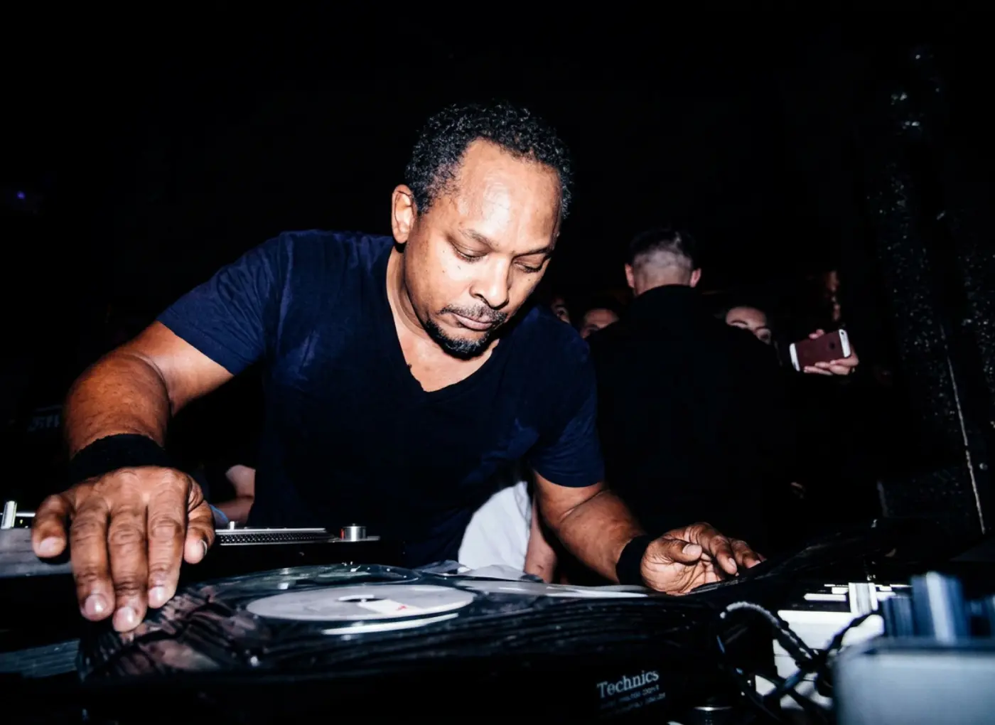 DJ mixing on vinyl turntables in a dark club, focused on the equipment and controls