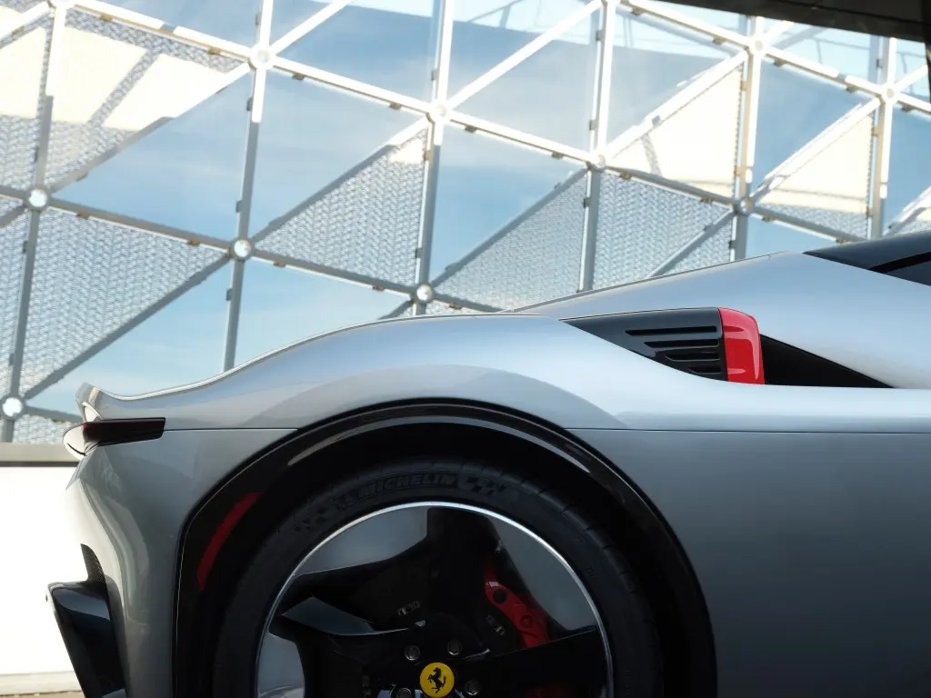 Ferrari se upravo pohvalio novim ljepotanom: SF90 Stradale pretvoren u futurističku berlinettu za američkog kupca's front wheel with a black alloy rim and red brake calipers, backdrop of glass architecture.