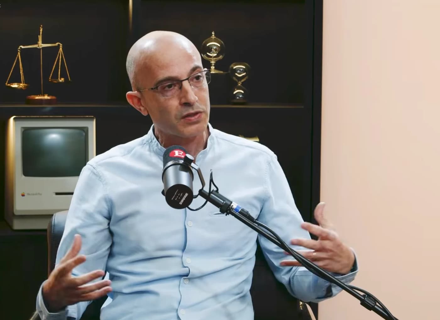 Man with glasses in a light blue shirt speaks into a professional microphone during a studio interview.