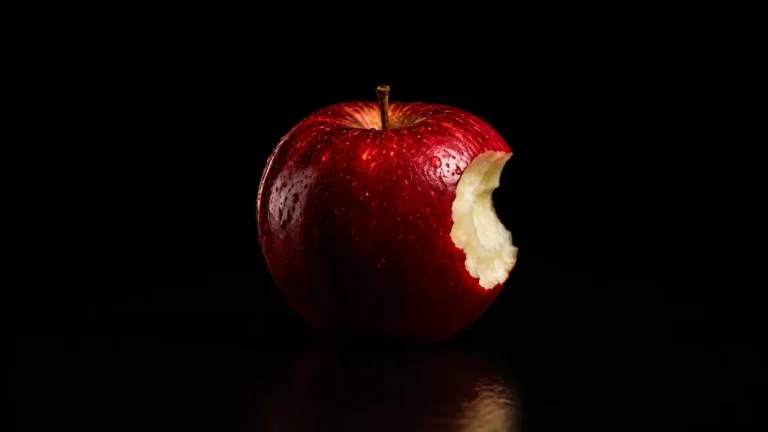 Red, glossy apple with a bite taken out of the right side, set against a black background with a reflective surface.
