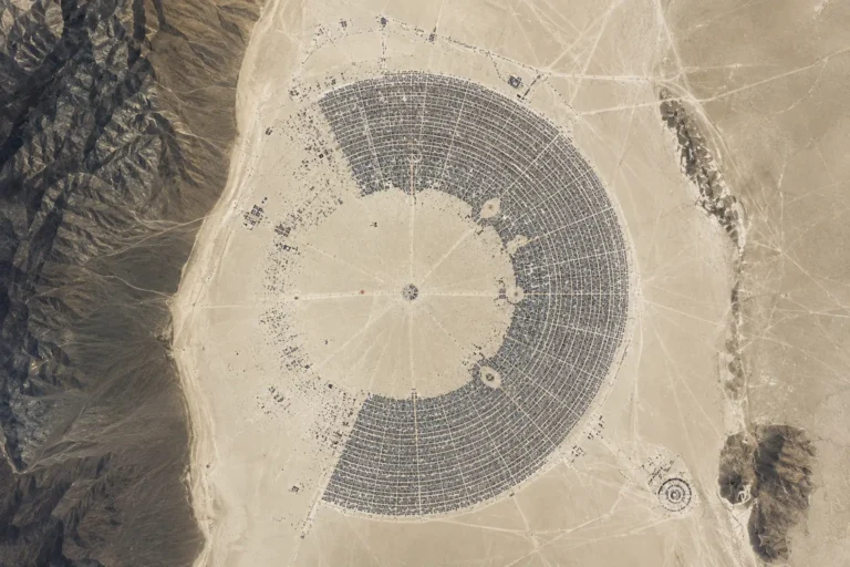 Aerial view of a circular solar farm with concentric rings of panels in a desert landscape.