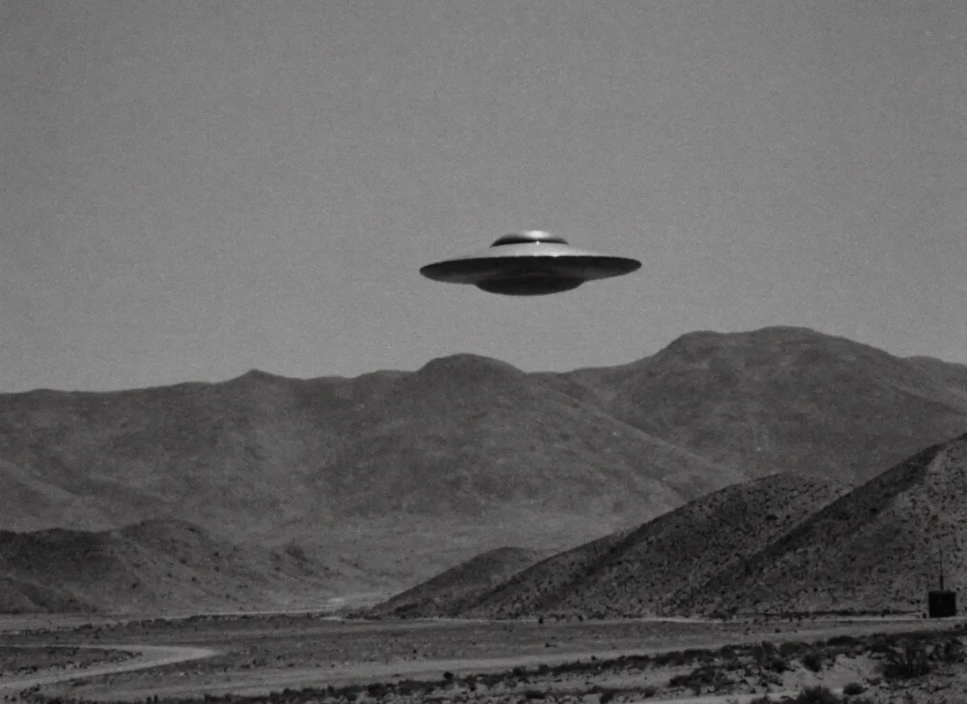 Silhouette of a classic flying saucer hovering above desert mountains in a black-and-white scene.