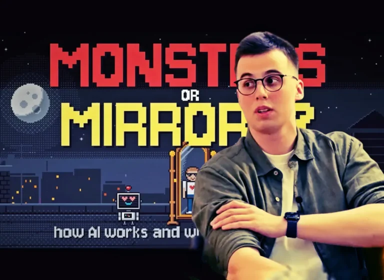 Man with short dark hair and glasses sits at a table in front of a pixel-art game backdrop with large red and yellow text, as if filming a video thumbnail.